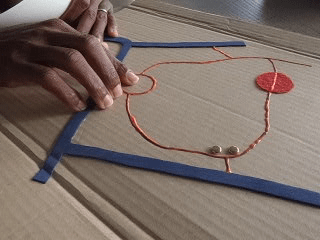 This is a cardboard map of her. It was used during mobility training. The main road is indicated in foam, and sideroads with coloured glue. A small forest is marked with fabric. The school where her kids go to has the entrance marked with two push pins