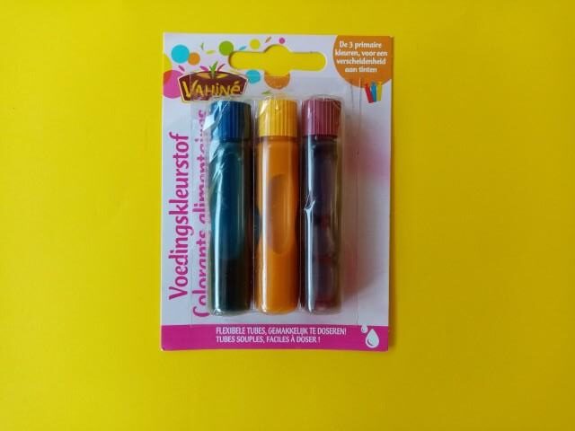Three bottles of food colorant inside of their packaging. The colors are blue, yellow and red.
