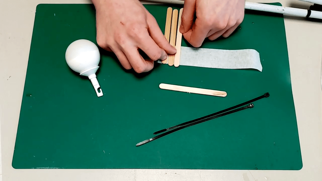Using a piece of tape to stick three wooden popsicle sticks next to each other.