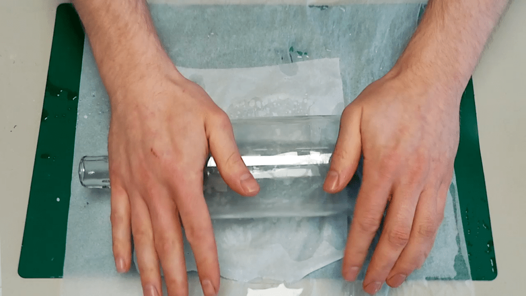 The baking paper is put on top of the material. A bottle is used to roll the material flat.