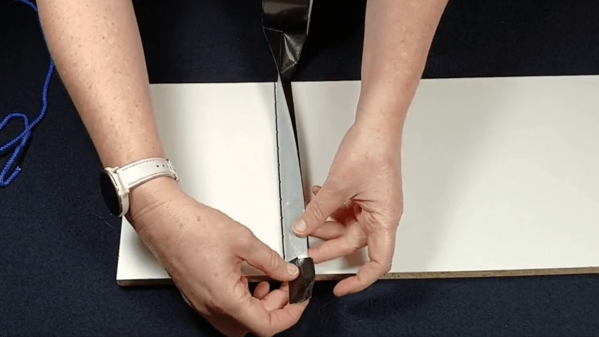 Using a piece of tape wrapped around itself, which is placed against the sticky side of the tape which hangs on the shelf.