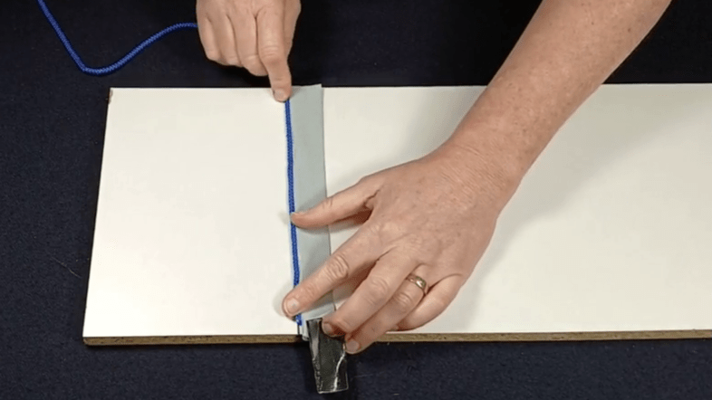 Placing the end of the string along the sticky edge of the tape.